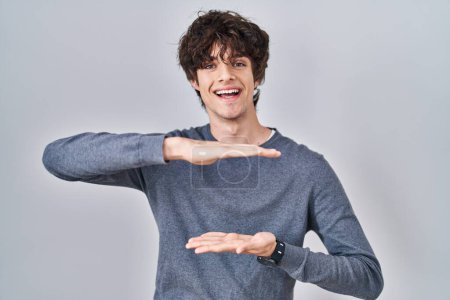 Foto de Young man standing over isolated background gesturing with hands showing big and large size sign, measure symbol. smiling looking at the camera. measuring concept. - Imagen libre de derechos