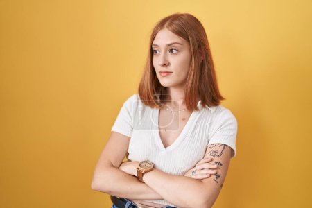Téléchargez les photos : Jeune rousse femme debout sur fond jaune regardant sur le côté avec les bras croisés convaincu et confiant - en image libre de droit