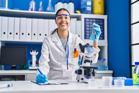 Photo for Young african american woman scientist analysing blood test tube writing report at laboratory - Royalty Free Image