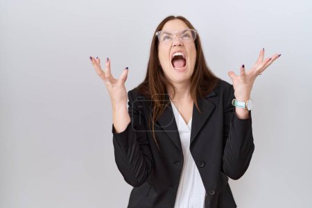 Téléchargez les photos : Beautiful brunette woman wearing business jacket and glasses crazy and mad shouting and yelling with aggressive expression and arms raised. frustration concept. - en image libre de droit