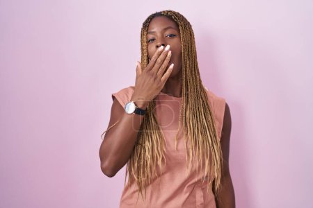 Foto de African american woman with braided hair standing over pink background bored yawning tired covering mouth with hand. restless and sleepiness. - Imagen libre de derechos
