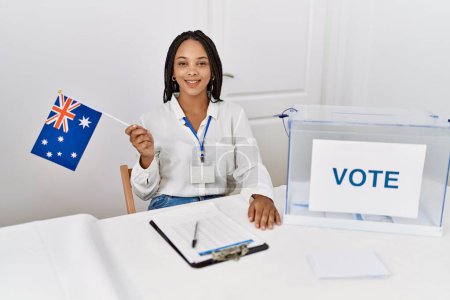 Photo for Young african american woman smiling confident holding australia flag working at electoral college - Royalty Free Image