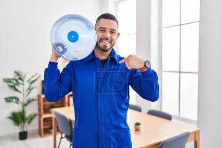 Foto de Hispanic service man holding a gallon bottle of water for delivery pointing finger to one self smiling happy and proud - Imagen libre de derechos