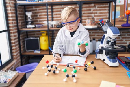 Photo for Adorable toddler student writing on notebook holding molecule at classroom - Royalty Free Image