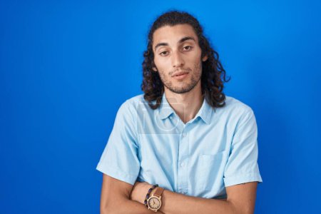 Photo for Young hispanic man standing over blue background looking sleepy and tired, exhausted for fatigue and hangover, lazy eyes in the morning. - Royalty Free Image