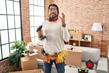 Photo for Handsome middle age man holding screwdriver at new home crazy and mad shouting and yelling with aggressive expression and arms raised. frustration concept. - Royalty Free Image