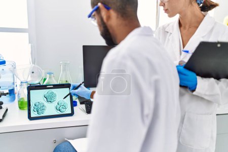 Foto de Man and woman scientist partners looking embryo image on touchpad at laboratory - Imagen libre de derechos