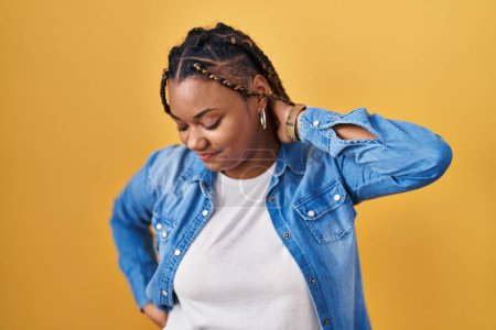 Photo for African american woman with braids standing over yellow background suffering of neck ache injury, touching neck with hand, muscular pain - Royalty Free Image