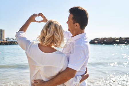 Foto de Middle age man and woman couple doing heart symbol with hands at seaside - Imagen libre de derechos