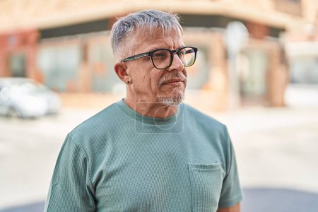 Téléchargez les photos : Homme aux cheveux gris d'âge moyen debout avec une expression sérieuse dans la rue - en image libre de droit