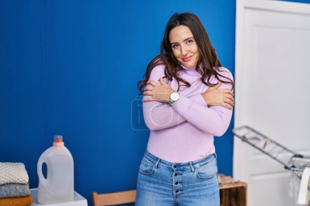 Téléchargez les photos : Young hispanic woman smiling confident hugging himself at laundry room - en image libre de droit