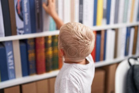 Foto de Adorable niño sosteniendo libro de estanterías en el aula - Imagen libre de derechos
