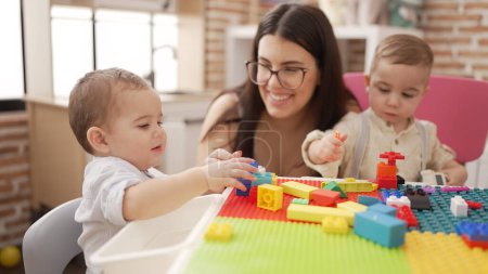 Photo for Teacher and preschool students playing with construction blocks sitting on table at kindergarten - Royalty Free Image