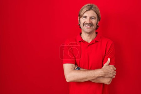 Téléchargez les photos : Caucasian man with mustache standing over red background happy face smiling with crossed arms looking at the camera. positive person. - en image libre de droit