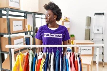 Téléchargez les photos : African young woman wearing volunteer t shirt at donations stand looking to side, relax profile pose with natural face with confident smile. - en image libre de droit