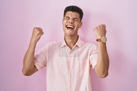 Photo for Young hispanic man standing over pink background celebrating surprised and amazed for success with arms raised and eyes closed. winner concept. - Royalty Free Image