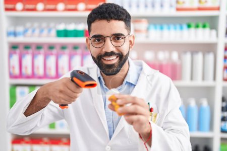 Foto de Hombre árabe joven farmacéutico escaneo píldoras botella en la farmacia - Imagen libre de derechos