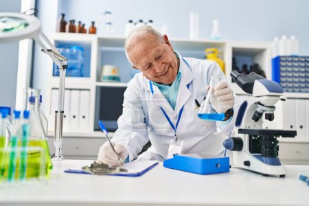 Téléchargez les photos : Homme senior portant un uniforme scientifique mesurant le liquide au laboratoire - en image libre de droit