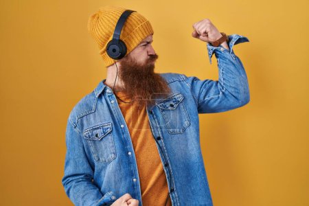 Photo for Caucasian man with long beard listening to music using headphones showing arms muscles smiling proud. fitness concept. - Royalty Free Image