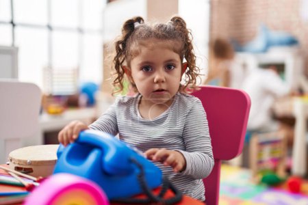 Téléchargez les photos : Adorable fille caucasienne jouant avec jouet téléphonique assis sur la table à la maternelle - en image libre de droit