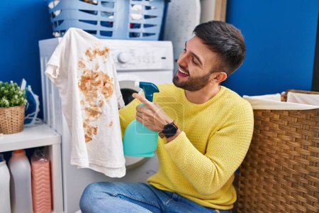 Photo for Young hispanic man cleaning stain using diffuser at laundry room - Royalty Free Image