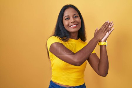 Téléchargez les photos : Young indian woman standing over yellow background clapping and applauding happy and joyful, smiling proud hands together - en image libre de droit