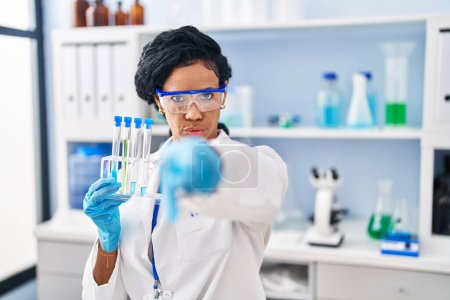 Photo for Middle age hispanic woman working at scientist laboratory pointing with finger to the camera and to you, confident gesture looking serious - Royalty Free Image