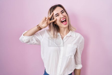Téléchargez les photos : Young beautiful woman standing over pink background doing peace symbol with fingers over face, smiling cheerful showing victory - en image libre de droit