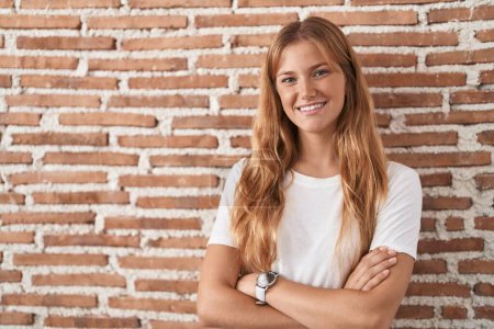 Téléchargez les photos : Young caucasian woman standing over bricks wall happy face smiling with crossed arms looking at the camera. positive person. - en image libre de droit