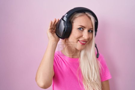 Photo for Caucasian woman listening to music using headphones smiling with hand over ear listening an hearing to rumor or gossip. deafness concept. - Royalty Free Image