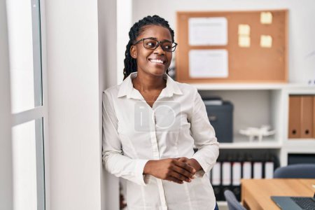 Téléchargez les photos : Afro-américaine femme d'affaires souriant confiant au bureau - en image libre de droit