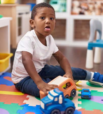 Photo for African american boy playing with cars and truck toy sitting on floor at kindergarten - Royalty Free Image