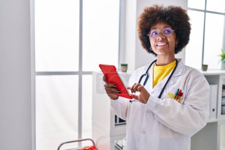Foto de Mujer afroamericana vistiendo uniforme médico usando touchpad en la clínica - Imagen libre de derechos