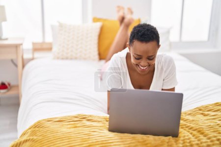 Foto de African american woman using laptop lying on bed at bedroom - Imagen libre de derechos