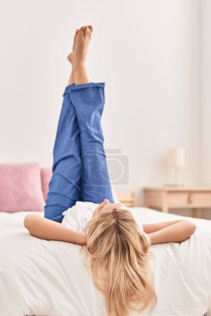 Téléchargez les photos : Young blonde woman lying on bed with legs raised up at bedroom - en image libre de droit