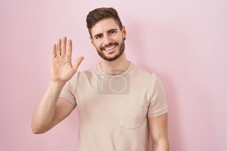 Téléchargez les photos : Homme hispanique avec barbe debout sur fond rose renonçant à dire bonjour heureux et souriant, geste de bienvenue amical - en image libre de droit