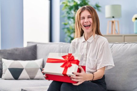 Foto de Beautiful woman holding gift winking looking at the camera with sexy expression, cheerful and happy face. - Imagen libre de derechos