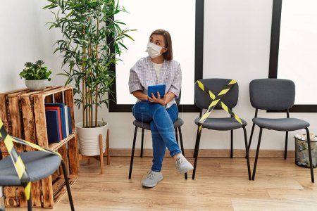 Photo for Middle age hispanic woman wearing safety mask using tablet at waiting room - Royalty Free Image