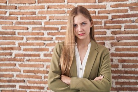 Photo for Young caucasian woman standing over bricks wall background skeptic and nervous, disapproving expression on face with crossed arms. negative person. - Royalty Free Image