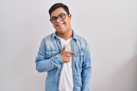 Téléchargez les photos : Jeune homme hispanique avec le syndrome du duvet portant une veste décontractée en denim sur fond blanc souriant joyeuse pointant avec la main et le doigt sur le côté - en image libre de droit