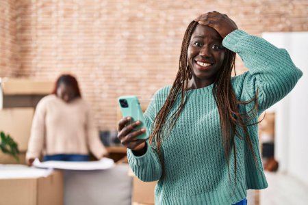 Foto de Mujer africana usando teléfono inteligente en el nuevo hogar estresado y frustrado con la mano en la cabeza, cara sorprendida y enojada - Imagen libre de derechos