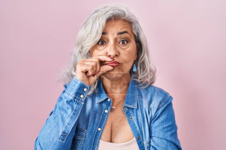 Foto de Middle age woman with grey hair standing over pink background mouth and lips shut as zip with fingers. secret and silent, taboo talking - Imagen libre de derechos