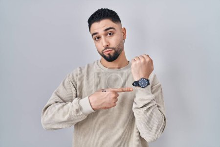 Photo for Young handsome man standing over isolated background in hurry pointing to watch time, impatience, looking at the camera with relaxed expression - Royalty Free Image