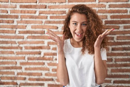 Photo for Young caucasian woman standing over bricks wall background celebrating crazy and amazed for success with arms raised and open eyes screaming excited. winner concept - Royalty Free Image