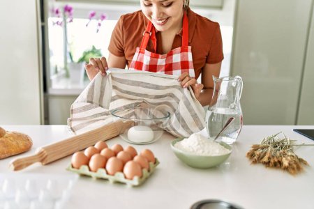 Téléchargez les photos : Young beautiful hispanic woman smiling confident covering bowl with bread dough at the kitchen - en image libre de droit