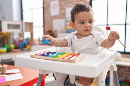 Photo for Adorable hispanic baby sitting on highchair playing xylophone at kindergarten - Royalty Free Image