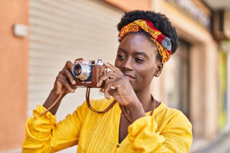 Téléchargez les photos : Jeune femme afro-américaine souriante confiante en utilisant une caméra vintage à la rue - en image libre de droit