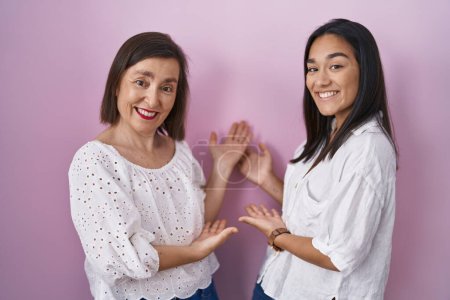 Téléchargez les photos : Hispanic mother and daughter together inviting to enter smiling natural with open hand - en image libre de droit
