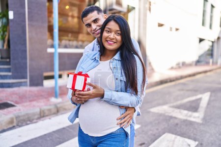 Téléchargez les photos : Young latin couple expecting baby surprise with gift at street - en image libre de droit
