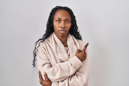 Foto de African woman standing over white background pointing with hand finger to the side showing advertisement, serious and calm face - Imagen libre de derechos